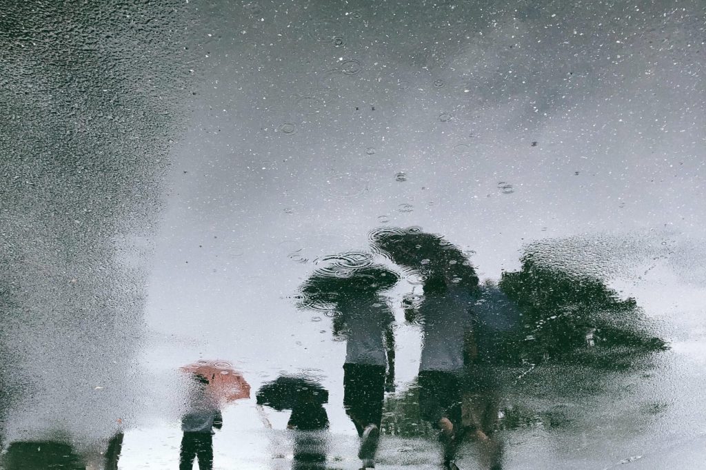 Image of reflection of people with umbrellas walking in the rain. 
Photo by Joey Huang on Unsplash