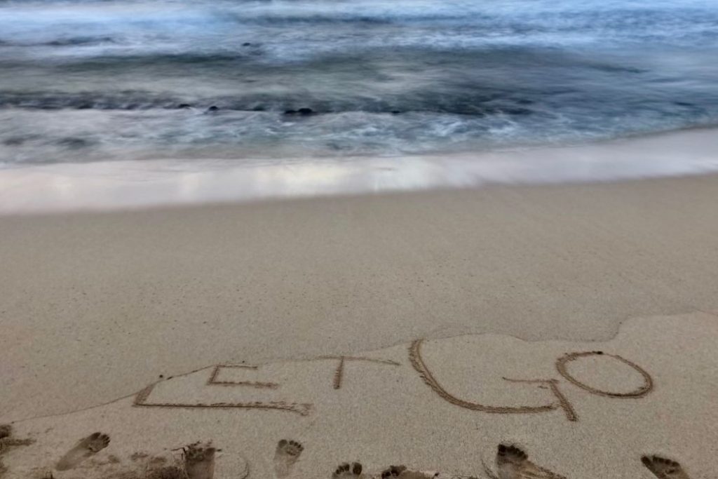 image of Let Go writing in sand, partially washed away by ocean in distance